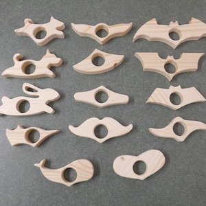 Puede incluir: Colección de sujetapáginas de madera en diversas formas: zorro, perro, conejo, ballena, bigote, corazón y murciélago. Cada uno tiene una abertura circular para el pulgar y es de madera clara.