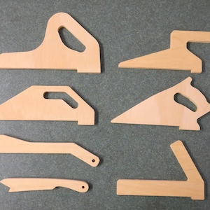 Könnte beinhalten: Eine Sammlung von sieben unfertigen Holzwerkzeugen, darunter verschiedene Formen von Griffen und Führungen. Die Werkzeuge sind hellbraun und scheinen neu zu sein, mit sauberen Kanten und glatten Oberflächen. Sie sind auf einer grauen Oberfläche angeordnet.