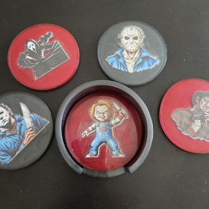 May include: Set of five round coasters featuring horror movie characters. The coasters have red and black backgrounds with images of Chucky, Freddy Krueger, Michael Myers, Jason Voorhees, and Ghostface.