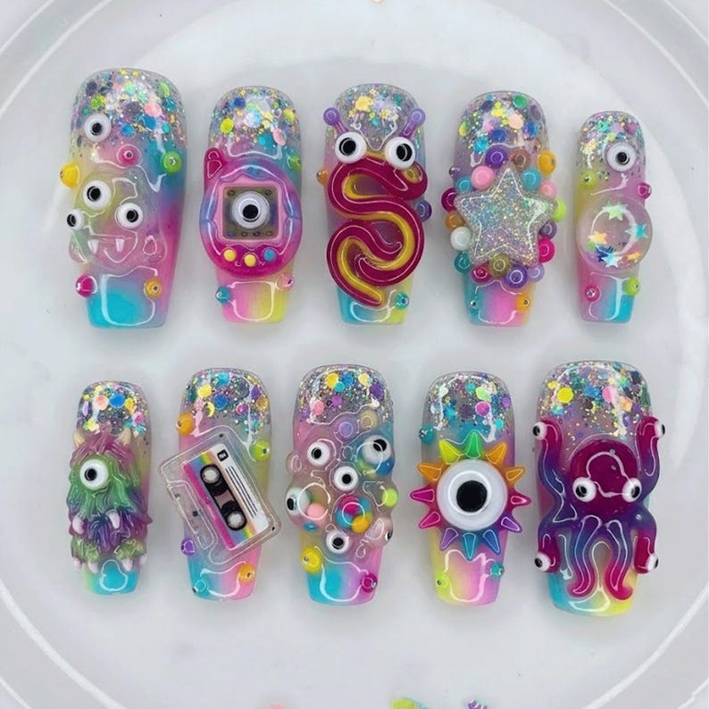May include: A set of twelve colorful, artistic fingernails with unique designs. Each nail features a different whimsical design, including googly eyes, a cassette tape, and a star, all set against a rainbow gradient background with glitter.