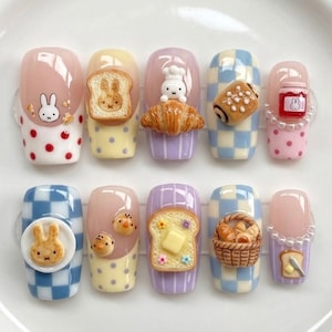 May include: A set of ten press-on nails featuring 3D charms including Miffy characters, toast, croissants, a jam jar, chicks, a bread basket, and buttered bread. The designs incorporate patterns like red and pink polka dots, blue and white checkers, and stripes.