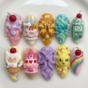 May include: A collection of ten artificial nails with colorful, cartoonish designs. The nails feature various themes, including ice cream, a castle, a bow, and cartoon characters. Each nail is adorned with intricate details and vibrant colors.