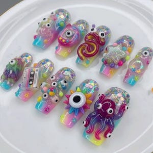 May include: A collection of colorful, artistic nail designs. Each nail features unique, whimsical embellishments, including googly eyes, a cassette tape, and an octopus. The nails are painted with a gradient of rainbow colors and glitter.
