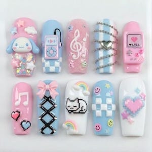 May include: A collection of ten artificial nails with various designs. The nails feature pastel pink and blue colors, with embellishments like a cartoon character, musical notes, a game console, and a pixelated cat. Some nails have glitter and decorative chains.