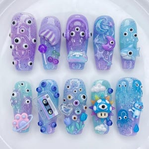 May include: A set of ten artificial nails with a variety of designs. The nails feature a gradient of purple and blue with various embellishments, including eyes, a shark, a cassette tape, and a mushroom.