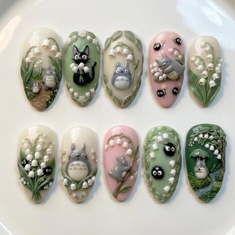 Puede incluir: Un conjunto de diez dise&ntilde;os de u&ntilde;as en forma de almendra. Cada u&ntilde;a presenta un dise&ntilde;o diferente, incluyendo los personajes de la pel&iacute;cula de animaci&oacute;n "Mi Vecino Totoro", con flores de lirio de los valles y escenas de bosque. La paleta de colores incluye blanco, verde, rosa y gris.