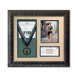 May include: Framed display with a marathon medal, race bib, and a photo of a runner. The medal is green and silver, and the bib number is 3195. The frame is dark brown with a textured pattern.