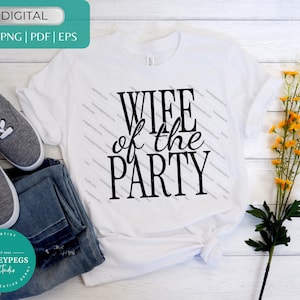 以下が含まれることがあります： 前面に黒い文字でWIFE of the PARTYとプリントされた白いTシャツ。グレーのスニーカー、青いデニムジーンズ、緑の葉がついた黄色い花の茎が、白い木製の表面に一緒に配置されています。