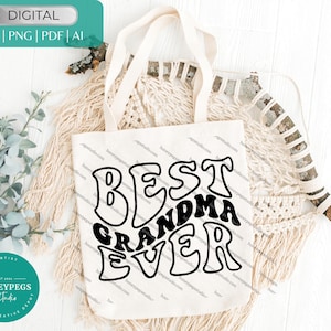 May include: A white tote bag with the text "BEST GRANDMA EVER" in black, retro-style lettering. The bag has long handles and is displayed on a neutral-toned background with decorative elements. The image also includes a teal graphic with text.