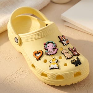 May include: A pale yellow clog shoe featuring a variety of colourful rubber charms attached to the ventilation holes. The charms include a pink axolotl with headphones, a heart-shaped dog, a corgi with a pan, a golden retriever, and a black cat.