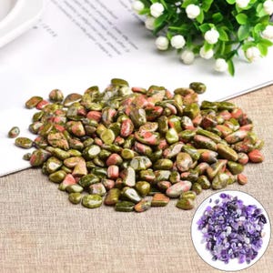 May include: A collection of polished unakite stones, displaying a blend of green, pink, and orange colours. The stones are of various sizes and shapes, with a smooth, rounded texture. A small pile of purple amethyst stones is in the lower right corner.