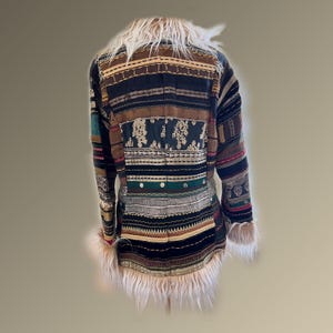 May include: A patchwork coat with a faux fur collar and cuffs. The coat features a variety of patterned fabrics in shades of brown, black, green, and red. The design includes embroidered details and horizontal stripes.