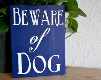 May include: A blue wooden sign with white lettering that reads "BEWARE of DOG".