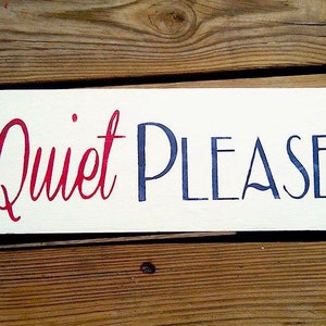 May include: A white wooden sign with the words "Quiet Please" written in red and blue paint.