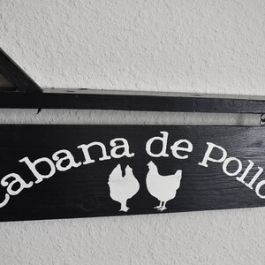 Puede incluir: Un letrero de madera negro con texto blanco que dice "Cabana de Pollo" con dos siluetas de pollo blancas.