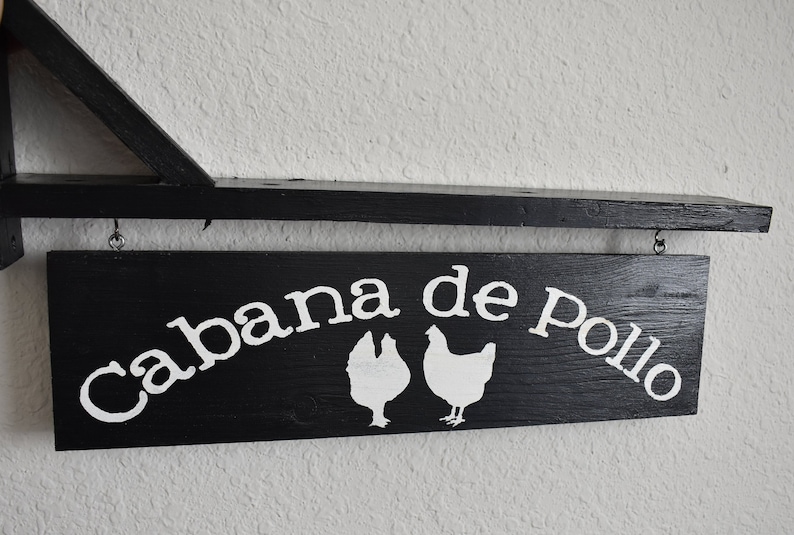 Puede incluir: Un letrero de madera negro con texto blanco que dice "Cabana de Pollo" con dos siluetas de pollo blancas.
