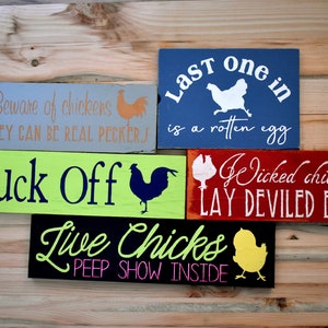 Puede incluir: Cinco letreros de madera con frases sobre pollos. Los letreros est&aacute;n pintados en varios colores, incluyendo verde, azul, rojo, negro y gris. Los letreros presentan diferentes siluetas de pollos y el siguiente texto: "Beware of chickens they can be real peckers", "Last one in is a rotten egg", "Cluck Off", "Wicked chickens lay deviled eggs", y "Live Chicks peep show inside".