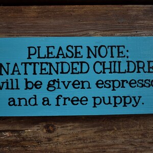 Pode incluir: Uma placa de madeira azul com o texto "PLEASE NOTE: UNATTENDED CHILDREN will be given espresso and a free puppy."