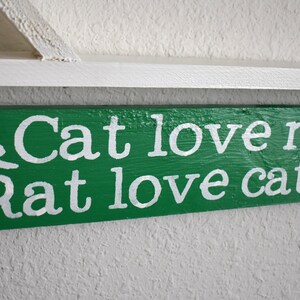 Puede incluir: Un letrero de madera verde con texto pintado en blanco y siluetas de un gato y una rata. El letrero dice "Cat love rat. Rat love cat."