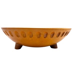 May include: A light brown wooden bowl with a smooth, rounded shape and a series of evenly spaced, shallow oval indentations carved along the upper exterior rim. The bowl is supported by three small, sturdy, dark brown wooden feet at the base.