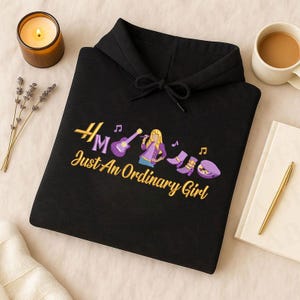 May include: Black hoodie with a musical theme. Features embroidered text and graphics in gold, purple, and other colors. The text reads "HM Just An Ordinary Girl". The graphics include a guitar, a singer, boots, and musical notes.