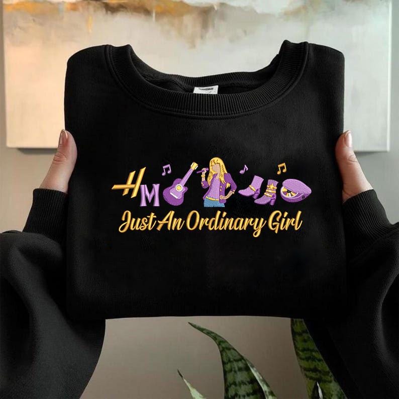May include: Black sweatshirt with the text "Hm Just An Ordinary Girl" in gold and a graphic of a woman with a microphone, guitar, boots, and a hat. The graphic is in purple, gold, and white.