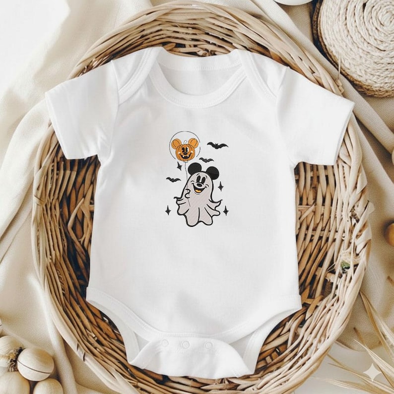 May include: A white short-sleeved baby bodysuit featuring a graphic print of a ghost wearing mouse ears, holding an orange pumpkin balloon with mouse ears, surrounded by small black bats and four-pointed star accents on the chest area.