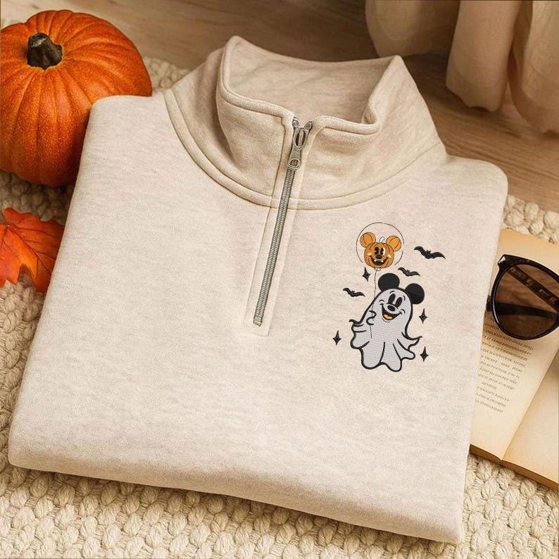 May include: A beige quarter-zip sweatshirt featuring a graphic of a ghost wearing Mickey Mouse ears and holding a pumpkin balloon, surrounded by small bats and stars. The sweatshirt has a high collar with a silver-toned metal zipper closure.