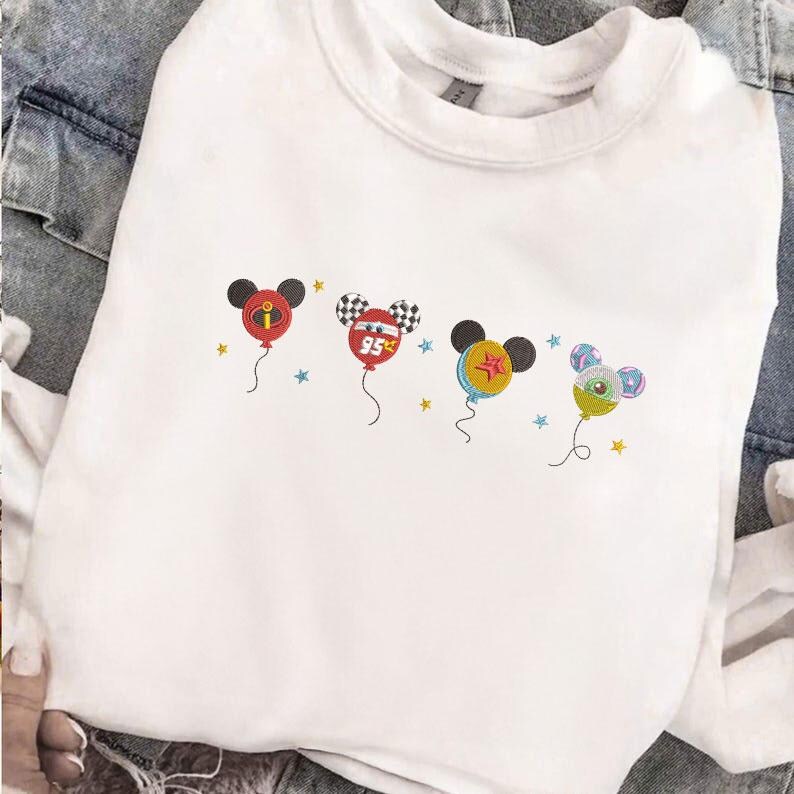 May include: White sweatshirt featuring embroidered Mickey Mouse-shaped balloons. Each balloon has a different design, including a red balloon with an "I" symbol, a checkered balloon with "95", a yellow balloon with a star, and a green balloon with a swirl.
