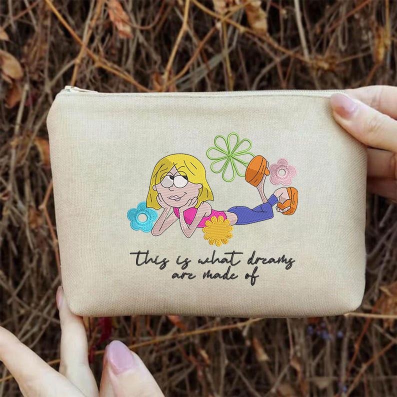 K&ouml;nnte beinhalten: Beige Canvas-Beutel mit Rei&szlig;verschluss. Der Beutel zeigt eine Cartoon-Illustration eines blonden M&auml;dchens, das liegt und von Blumen umgeben ist. Der Text "This is what dreams are made of" ist darunter gedruckt.