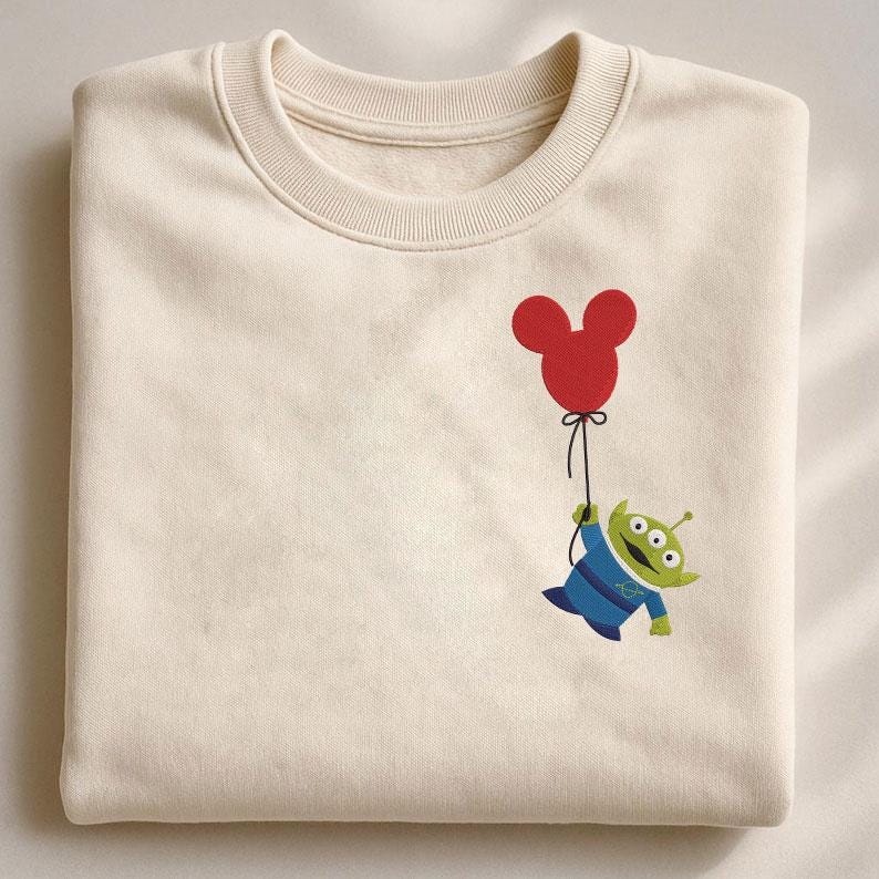 May include: Cream-coloured sweatshirt with a cartoon alien holding a red Mickey Mouse balloon. The alien is green with three eyes and wears a blue uniform. The balloon is tied with a black string.