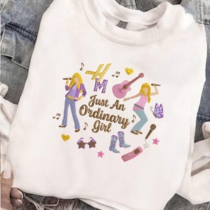 Puede incluir: Sudadera blanca con un gr&aacute;fico colorido que presenta dos figuras de dibujos animados, notas musicales y el texto "Just An Ordinary Girl". El dise&ntilde;o incluye una guitarra, un micr&oacute;fono y otros elementos musicales.