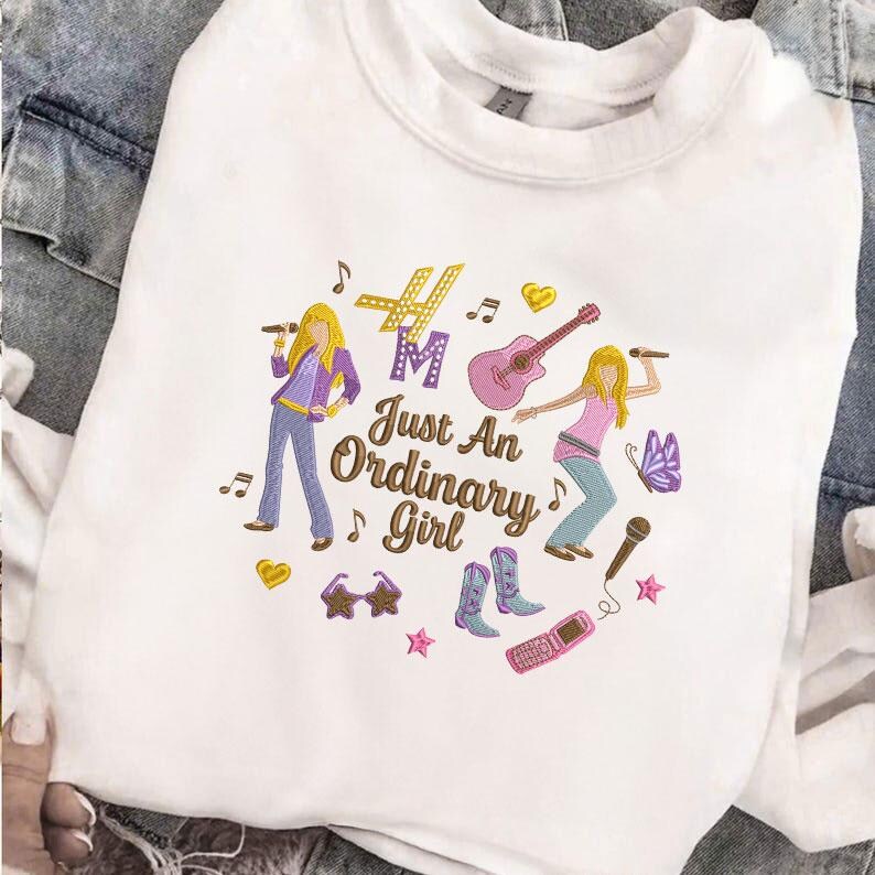 Puede incluir: Sudadera blanca con un gr&aacute;fico colorido que presenta dos figuras de dibujos animados, notas musicales y el texto "Just An Ordinary Girl". El dise&ntilde;o incluye una guitarra, un micr&oacute;fono y otros elementos musicales.