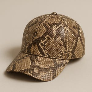 Puede incluir: Gorra de béisbol con estampado de piel de serpiente en tonos marrón y beige. La gorra tiene una visera curva y un pequeño botón en la parte superior. El sombrero está hecho de un material texturizado.