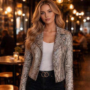 May include: A woman in a snakeskin-effect jacket, white top, and black jeans. The jacket is a biker style with a notched collar and an asymmetrical zip. A black belt with a gold buckle is worn at the waist.