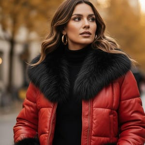 May include: A red puffer jacket with a black fur collar and cuffs. The jacket is worn over a black turtleneck. The person is wearing gold hoop earrings. The background is blurred, with autumn colors.