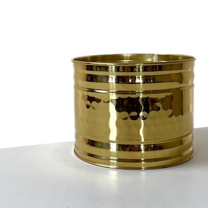 May include: A gold hammered metal planter with a round shape and a slightly flared rim. The planter has a textured surface and a shiny finish.