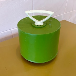 May include: A green plastic container with a white handle on top. The container has a round shape and a smooth surface.