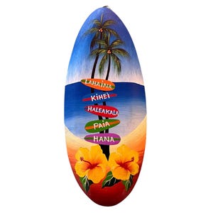 May include: A wooden surfboard painted with a blue sky, palm trees, and a beach scene. The surfboard has five signs pointing to different locations in Hawaii: Lahaina, Kihei, Haleakala, Paia, and Hana.