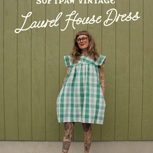 May include: A green and white checked Laurel House Dress from Softpaw Vintage. The dress features short sleeves and a relaxed fit. The words "SOFTPAW VINTAGE" and "Laurel House Dress" are written in white script above the dress.