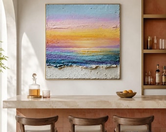 May include: A square canvas painting featuring a textured impasto seascape at sunset. The composition displays horizontal bands of light blue, soft pink, and vibrant yellow sky above a deep blue and purple ocean, finished with a white sandy shore.