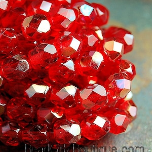 May include: A close-up of a cluster of red faceted glass beads. The beads are arranged in a random pattern and have a shiny, reflective surface.