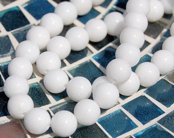 Puede incluir: Una hebra de cuentas blancas hechas de piedras lisas, redondas, opacas y blancas. Las cuentas están enhebradas en un hilo transparente y están dispuestas en un patrón circular. Las cuentas están sobre una superficie de azulejos azules y blancos.