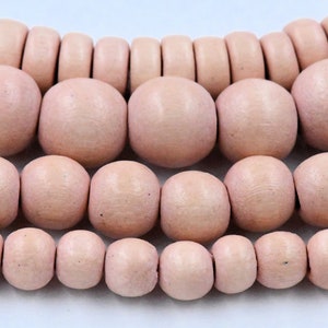 May include: A strand of wooden beads in various sizes, all in a pale pink colour. The beads are round and smooth, with a slightly textured surface.