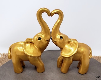 Può includere: Topper per torta a forma di elefante dorati, con le proboscidi degli elefanti che formano un cuore. Gli elefanti si guardano e hanno gli occhi neri.