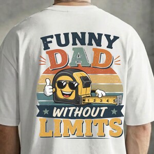 May include: A white t-shirt featuring a graphic on the back with the text FUNNY DAD WITHOUT LIMITS. The design includes a yellow tape measure character wearing black sunglasses, giving a thumbs up, set against a retro sunset background.