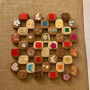 May include: A square trivet constructed from interconnected wooden blocks, each featuring unique embellishments including colourful plastic squares, sequins, rhinestones, and butterfly shapes. Some blocks are stamped with text like YUM and thank you.