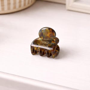 Könnte beinhalten: Eine kleine Haarspange im Schildpattmuster. Die Spange ist eine Mischung aus Braun, Gelb und Schwarz, mit dem Text "FRANCE Handmade" auf der Vorderseite. Die Spange ist so konzipiert, dass sie das Haar an Ort und Stelle hält.