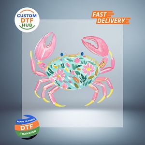 May include: A watercolor illustration of a crab with pink claws and legs, and a turquoise body adorned with pink flowers and green leaves. The image includes the text "CUSTOM DTF HUB" and "FAST DELIVERY".