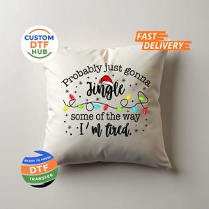May include: Cream-colored square pillow with the text "Probably just gonna Jingle some of the way I'm tired." The text is in black with a Santa hat on the word "Jingle" and a string of Christmas lights.